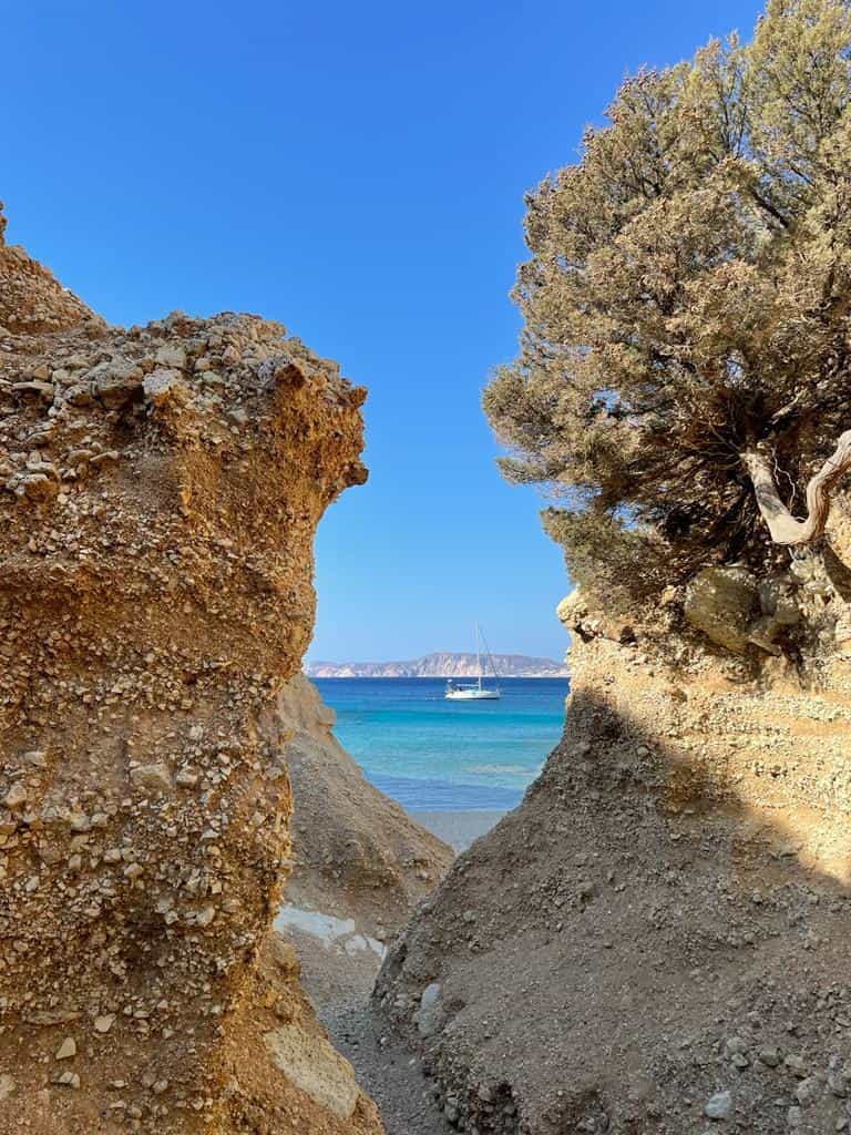Una barca a vela vista da terra tra le rocce di Milos